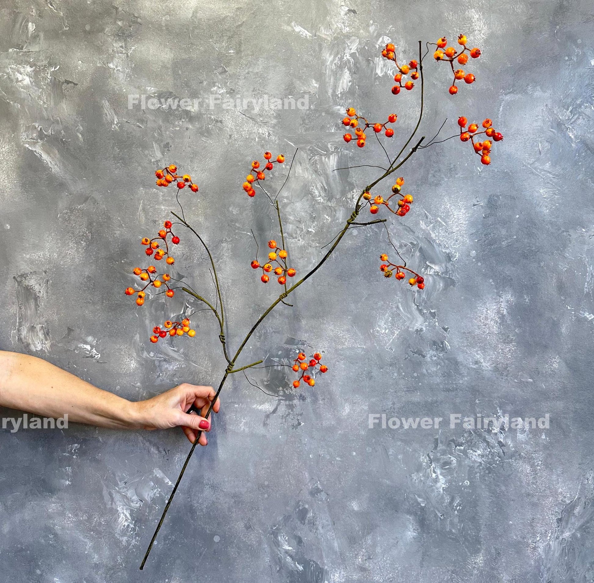 Hand holding a 43 inch faux orange berry branch showing full length