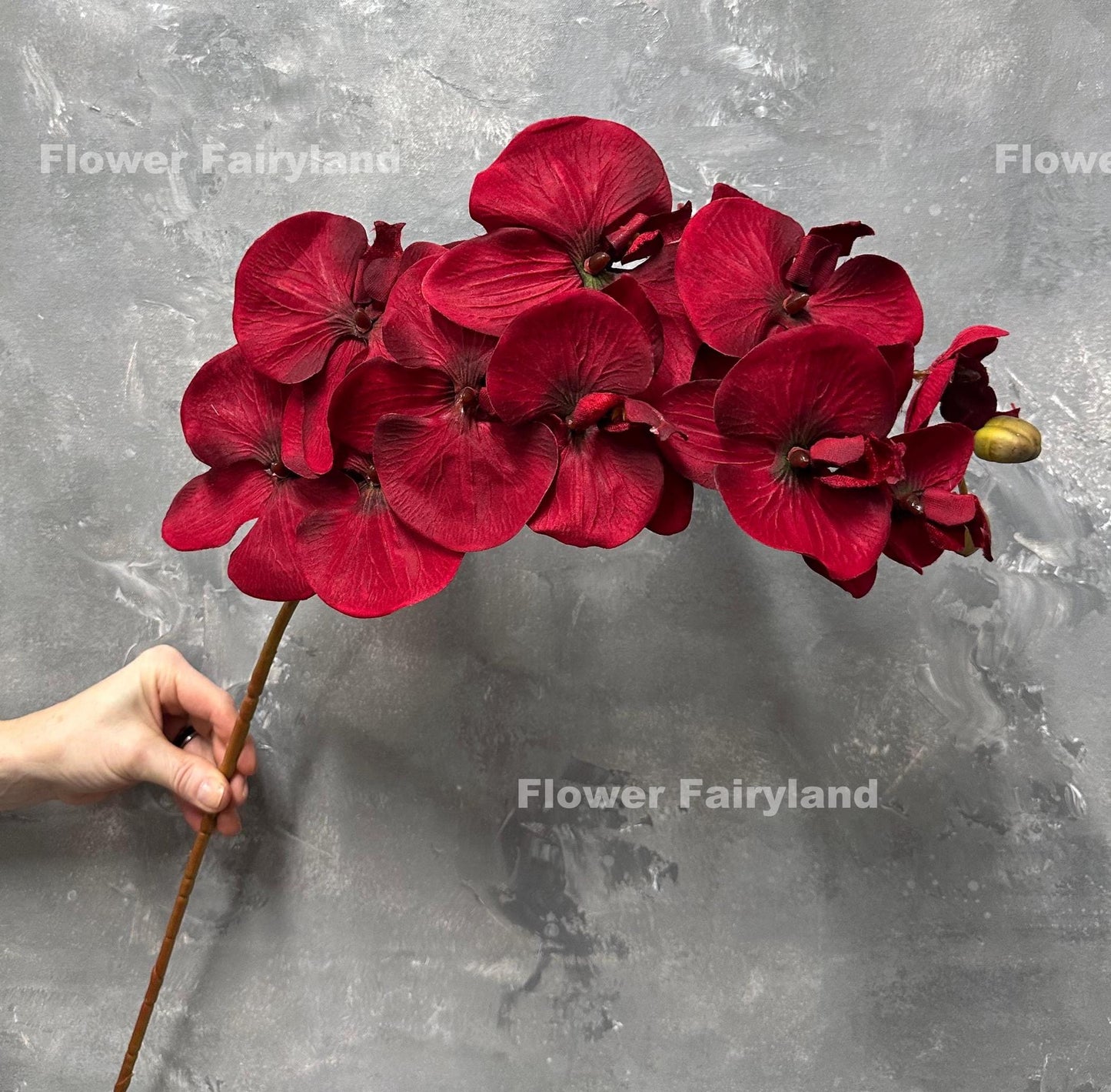 Deep red faux orchid stem held in hand