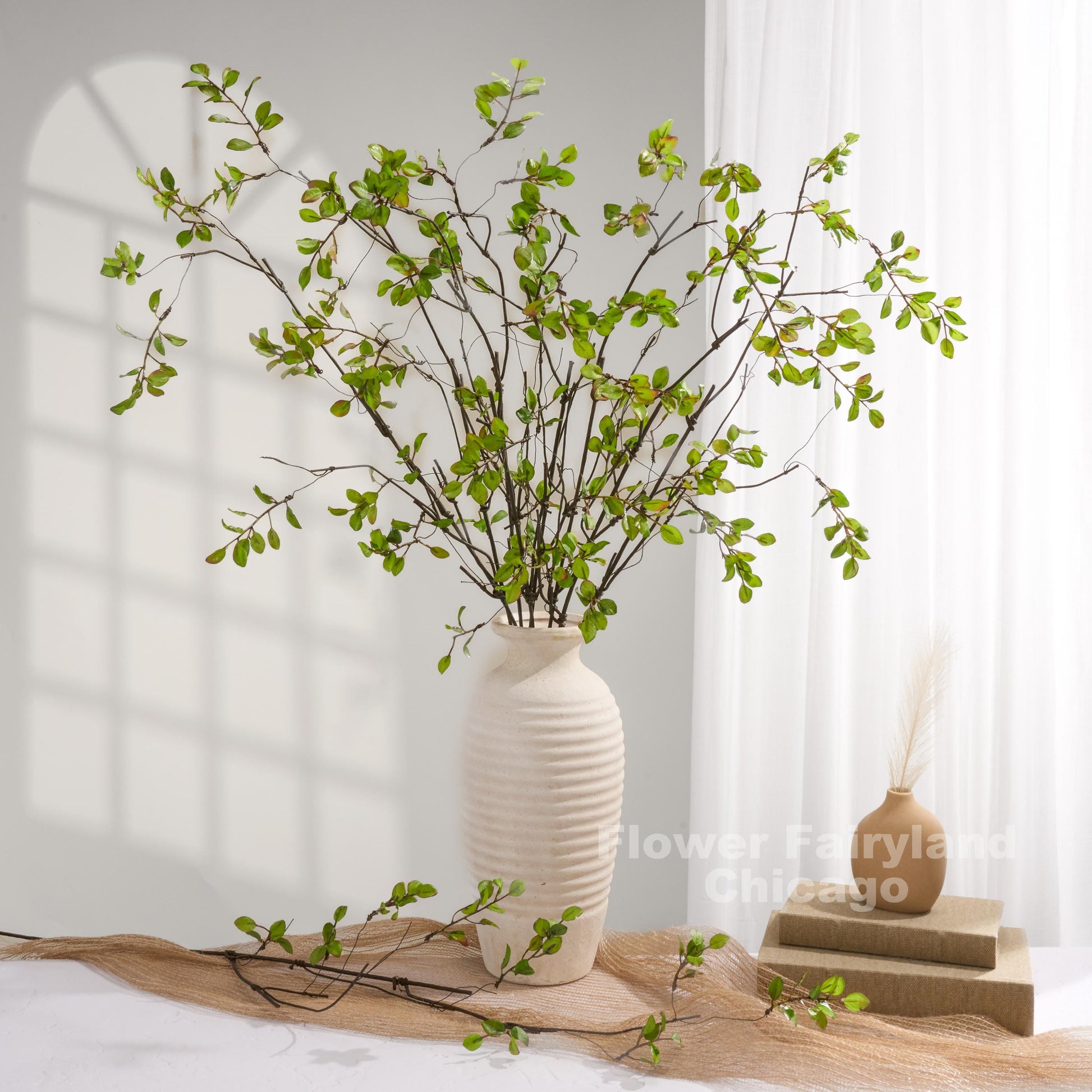 Green faux leaf branch arrangement in vase with books
