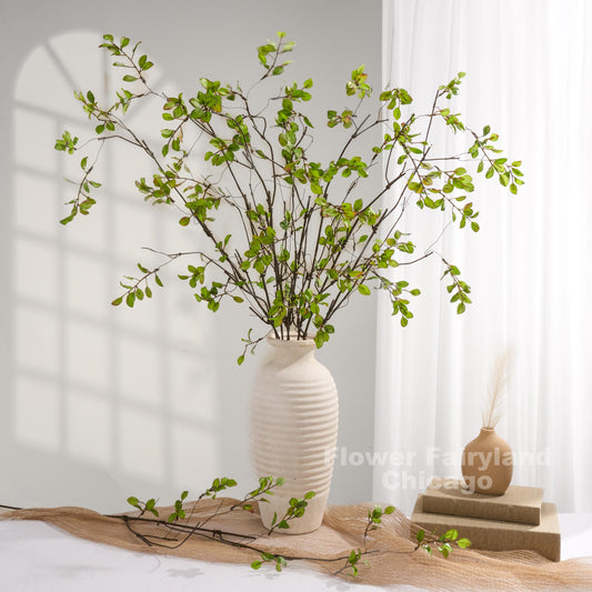 Green faux leaf branch arrangement in vase with books