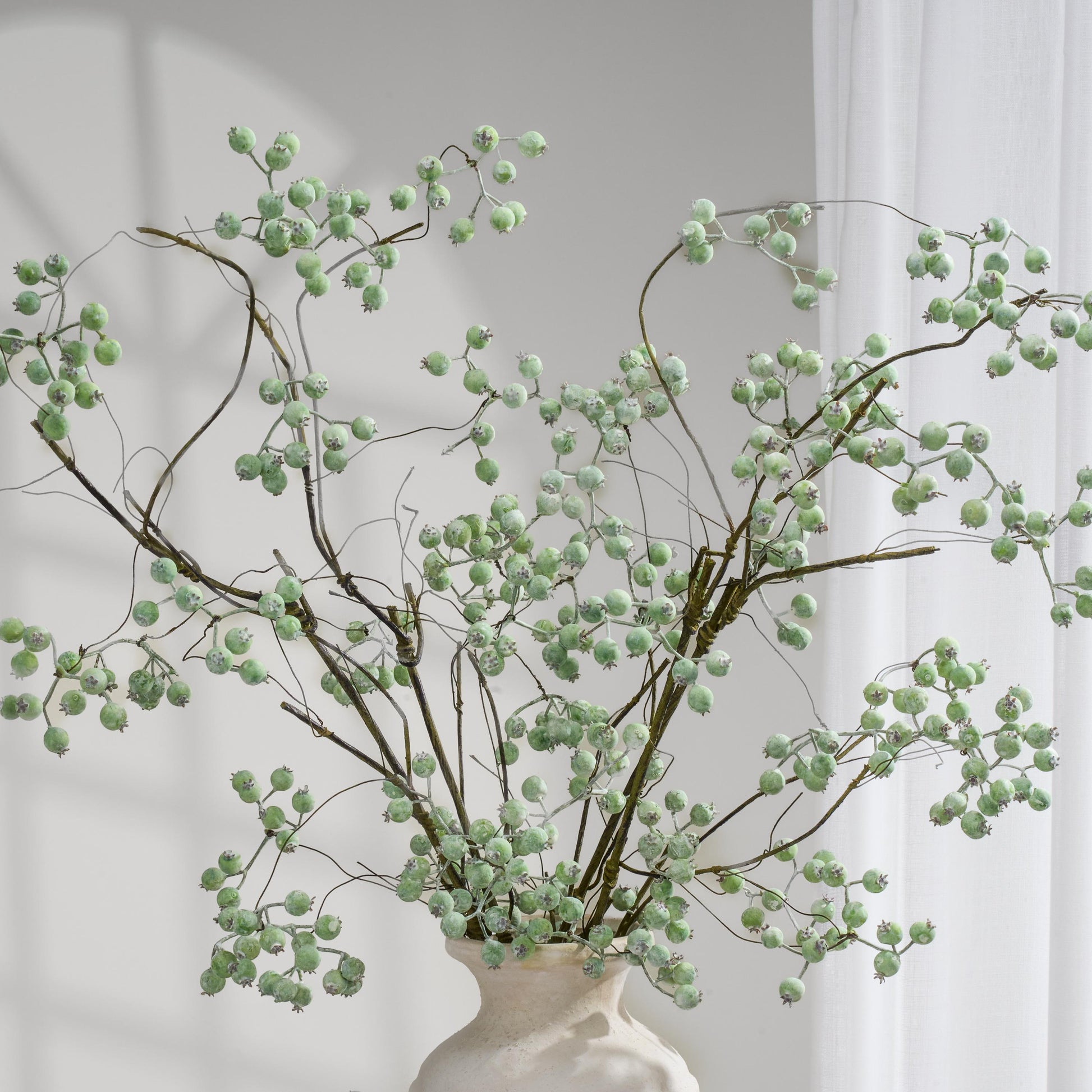 Dusty green faux berry branches arranged in a cream vase