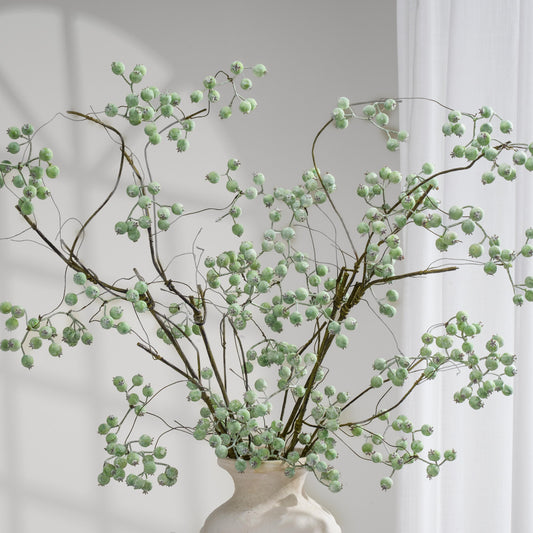 Dusty green faux berry branches arranged in a cream vase