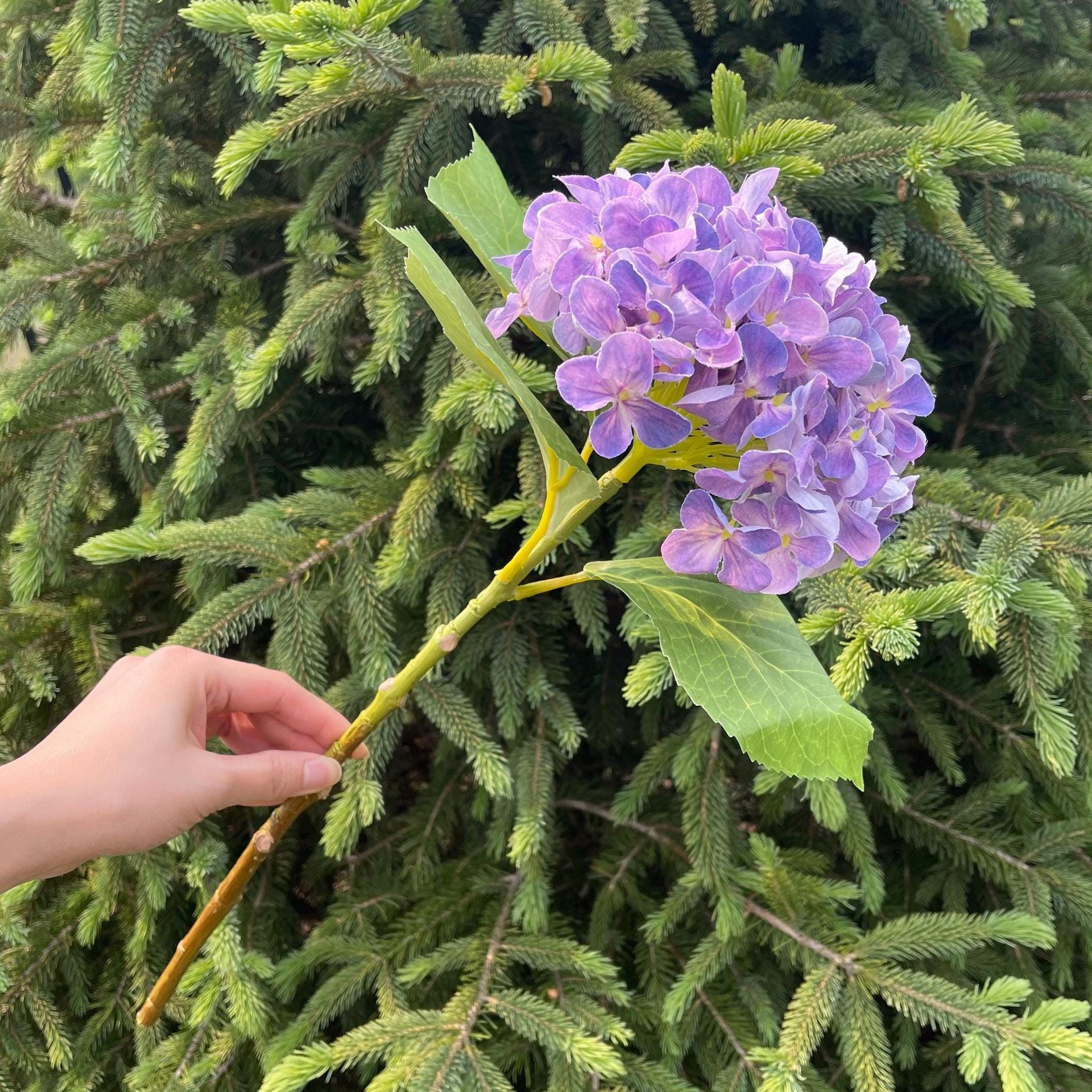 Purple faux hydrangea stem held in hand