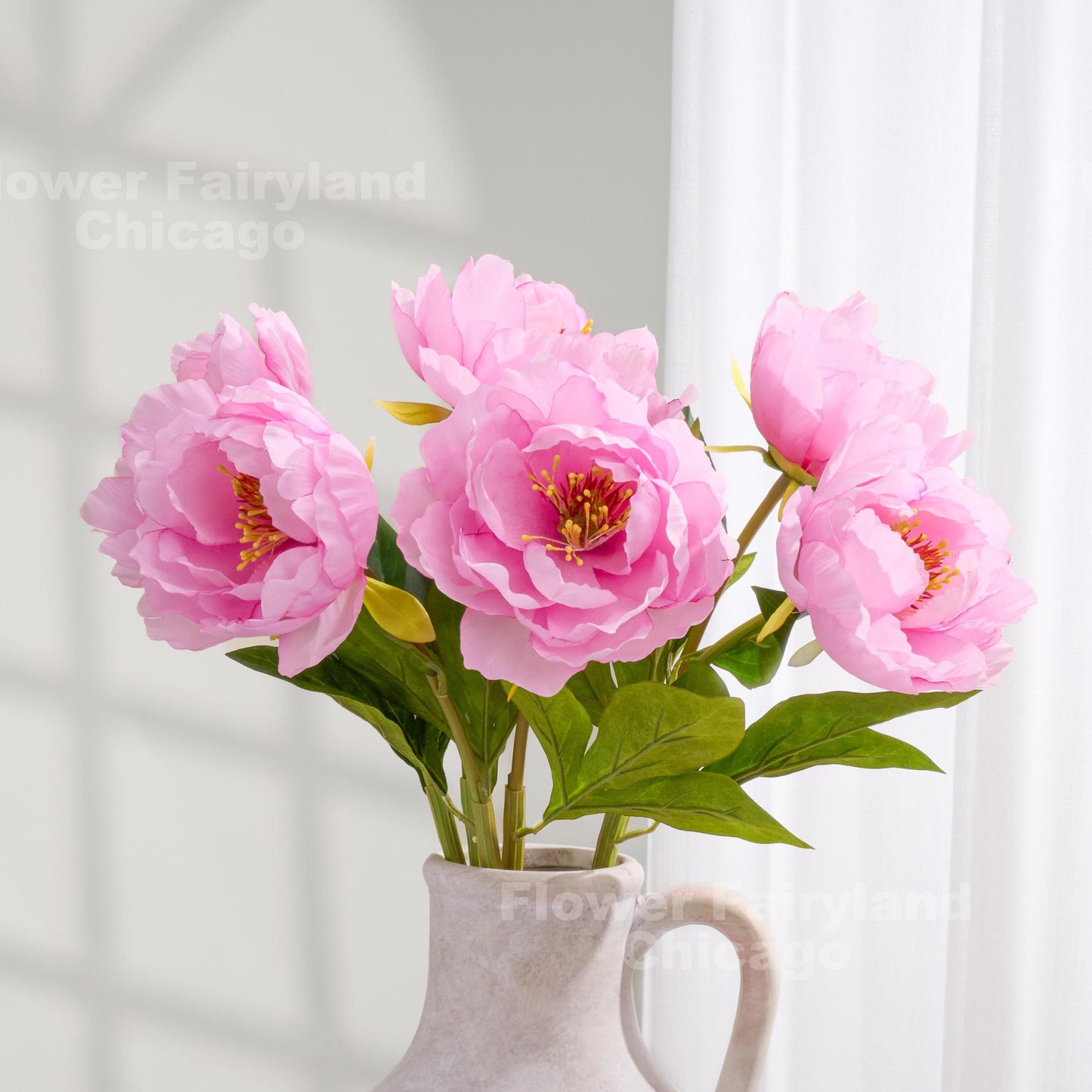 Pink faux peonies styled in a clear pitcher vase