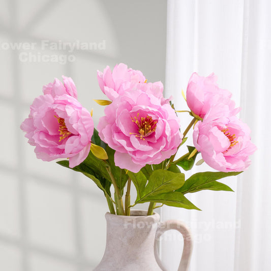 Pink faux peonies styled in a clear pitcher vase