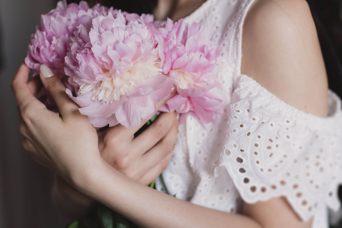 Woman in white lace dress holding pale pink peonies