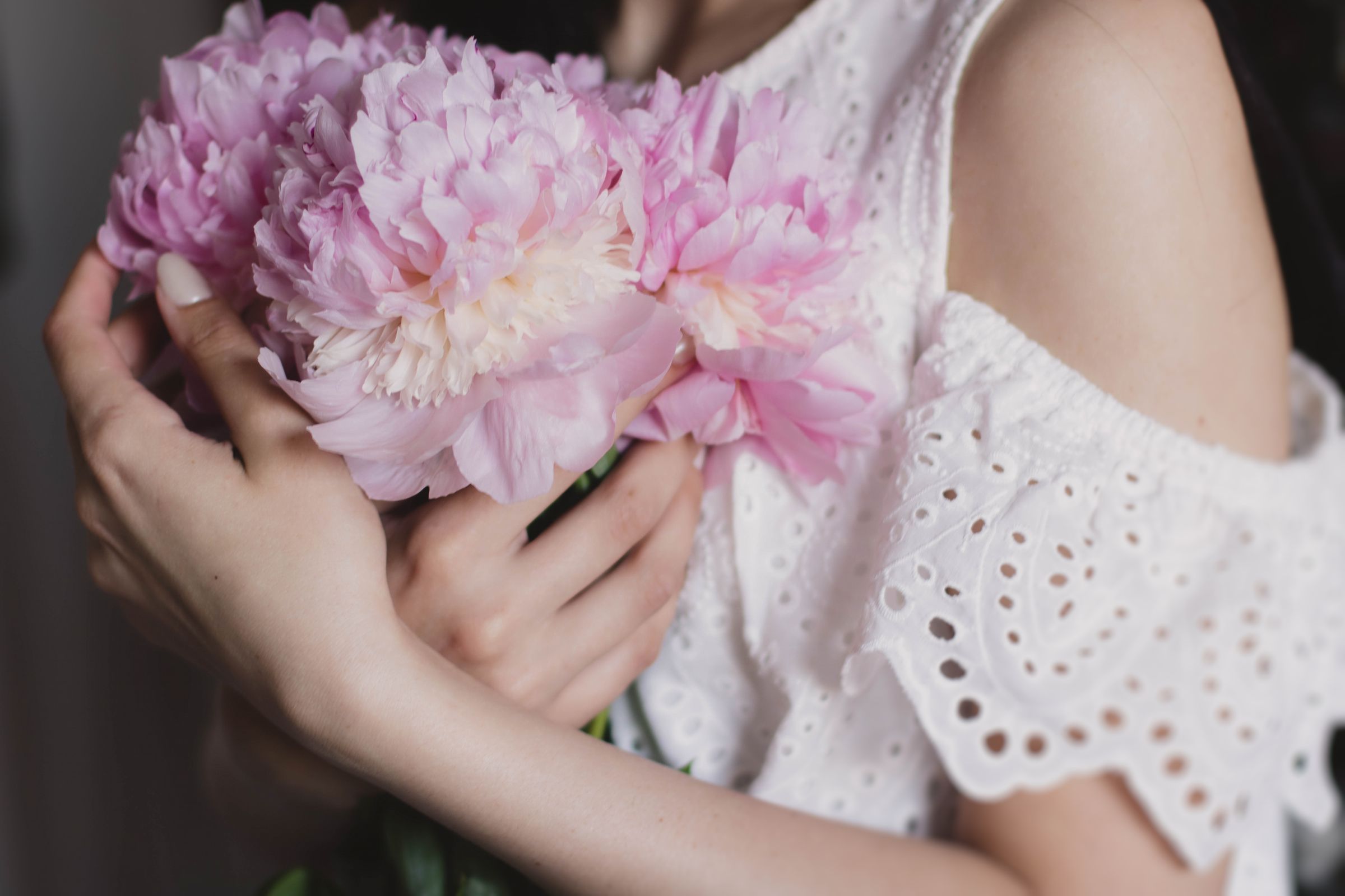 Woman in white lace dress holding pale pink peonies